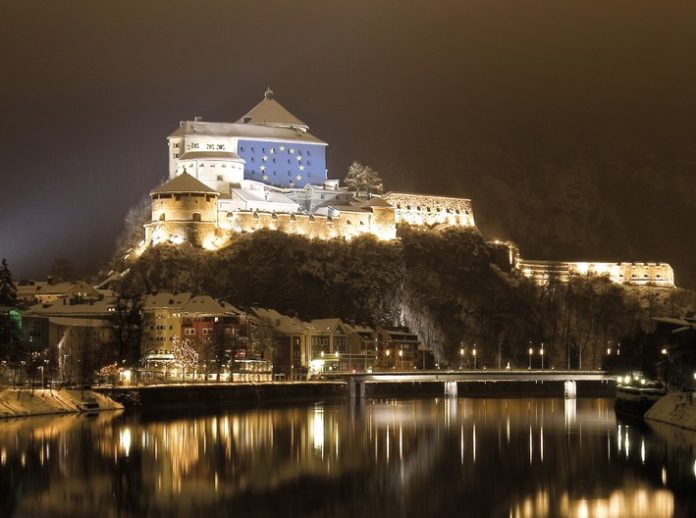 Kufstein, die Perle am grünen Inn, ist historisch eng mit dem angrenzenden Bayern verbunden. Die Festung Kufstein war Jahrhunderte lang das Objekt der Begierde zahlreicher Grenzstreitigkeiten. Das Kufsteinerland wurde erst 1814 dauerhaft Tirol zugesprochen. 
                
                
                  In Kufstein selbst wird ein freundschaftliches Verhältnis zum deutschen Nachbarn gelebt, und besonders jetzt in der Zeit der Grenzschließungen und Ausgangssperren merkt man auf beiden Seiten der Grenze, wie sehr diese Verbindung nun fehlt.
                
                
                   Aus diesem Grund setzt Kufstein ein leuchtendes Zeichen ? am 7. Mai um 21 Uhr wird auf die Festung die EU-Flagge projektiert. Die Festung Kufstein selbst öffnet am 30. Mai 2020 wieder ihre Pforten für Besucher.
                
              Die Sterne des EU-Emblems stehen für die Zusammengehörigkeit, die für die Kufsteiner Bevölkerung, den Handel und nicht zuletzt den Tourismus integraler Bestandteil des täglichen Lebens war und ist. Mit Corona wurde die so gewohnte Reisefreiheit abrupt verändert ? plötzlich wurde angehalten, kontrolliert und auch gestraft. Für das offene und gesellige Volk des Kufsteinerlandes und seine Nachbarn ein herber Schlag.Lena Maier aus Erl erzählt: ?Wer direkt an der Grenze wohnt wie wir, lebt eigentlich auf beiden Seiten. Die Grenze existierte für uns immer nur theoretisch und jeder hat Freunde, Verwandte auf der ?anderen Seite?. Normalerweise besuche ich meine beste Freundin in Oberaudorf mit dem Rad und nehme einfach die Holzbrücke über den Inn. Von einem Tag auf den anderen war der Übergang mit einem Holzverschlag dichtgemacht. Ein eigenartiges Gefühl sich nicht mehr nah sein zu können.?Erl liegt direkt an der Grenze und am Kranzhorn steht man mit einem Bein auf deutschem und mit dem anderen auf österreichischem Boden. So wie Lena geht es vielen im Kufsteinerland. Durch die Grenzschließung wurde so manc...